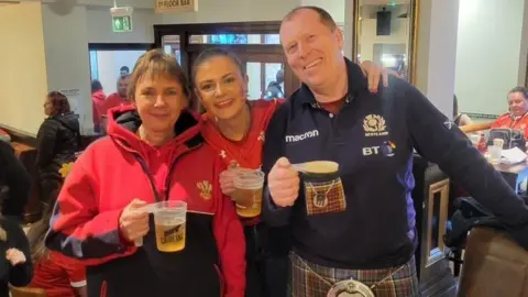 Francesca Murphy Francesca stands in a pub between her mum and dad. They are all smiling and looking happy and holding pints of beer.