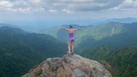 Francesca Murphy Francesca Murphy stands on a hill overlooking a beautiful view of green, lush mountains. Her back is to the camera and she looks at the scene with her arms outstretched. 