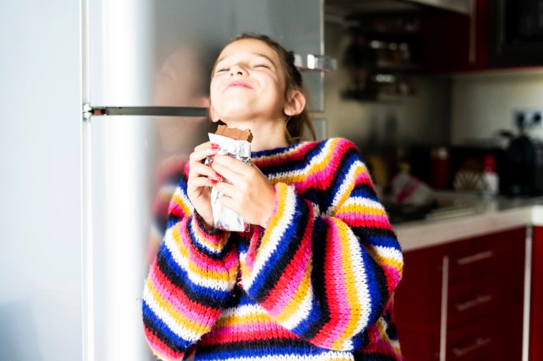 Girl in striped pullover eating chocolate in home kitchen