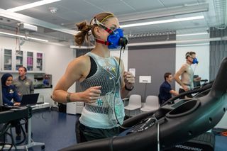 A photo of a woman wearing a Samsung Galaxy Watch running on a treadmill wearing an oxygen mask.