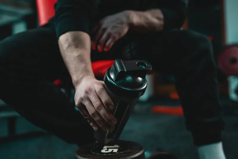 Close-up of a man sitting in a gym holding a black reusable water bottle.